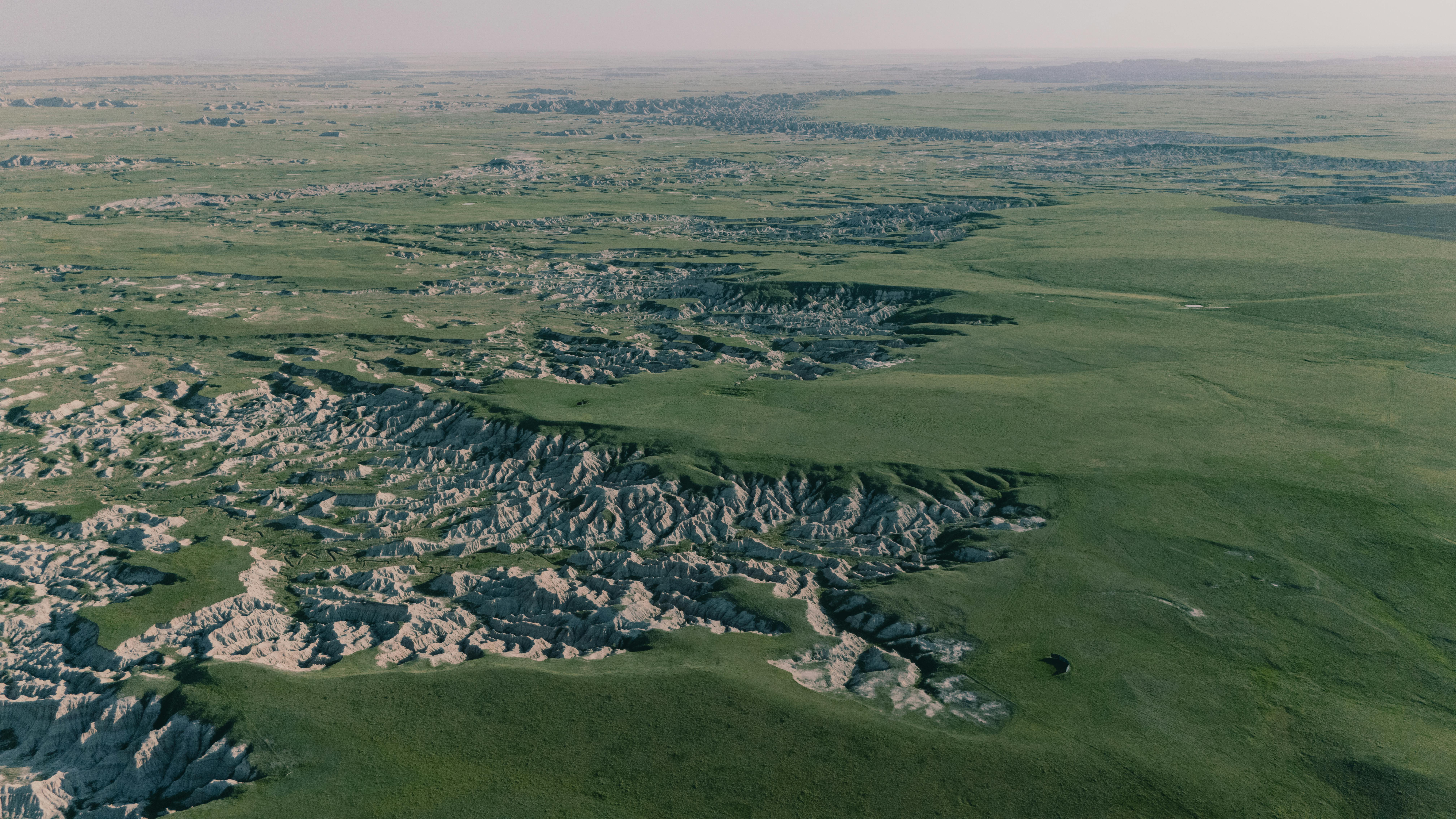 Kostenlos Malerische Luftaufnahme des Badlands-Nationalparks mit ausgedehnten Graslandschaften und schroffen Klippen. Stock-Foto