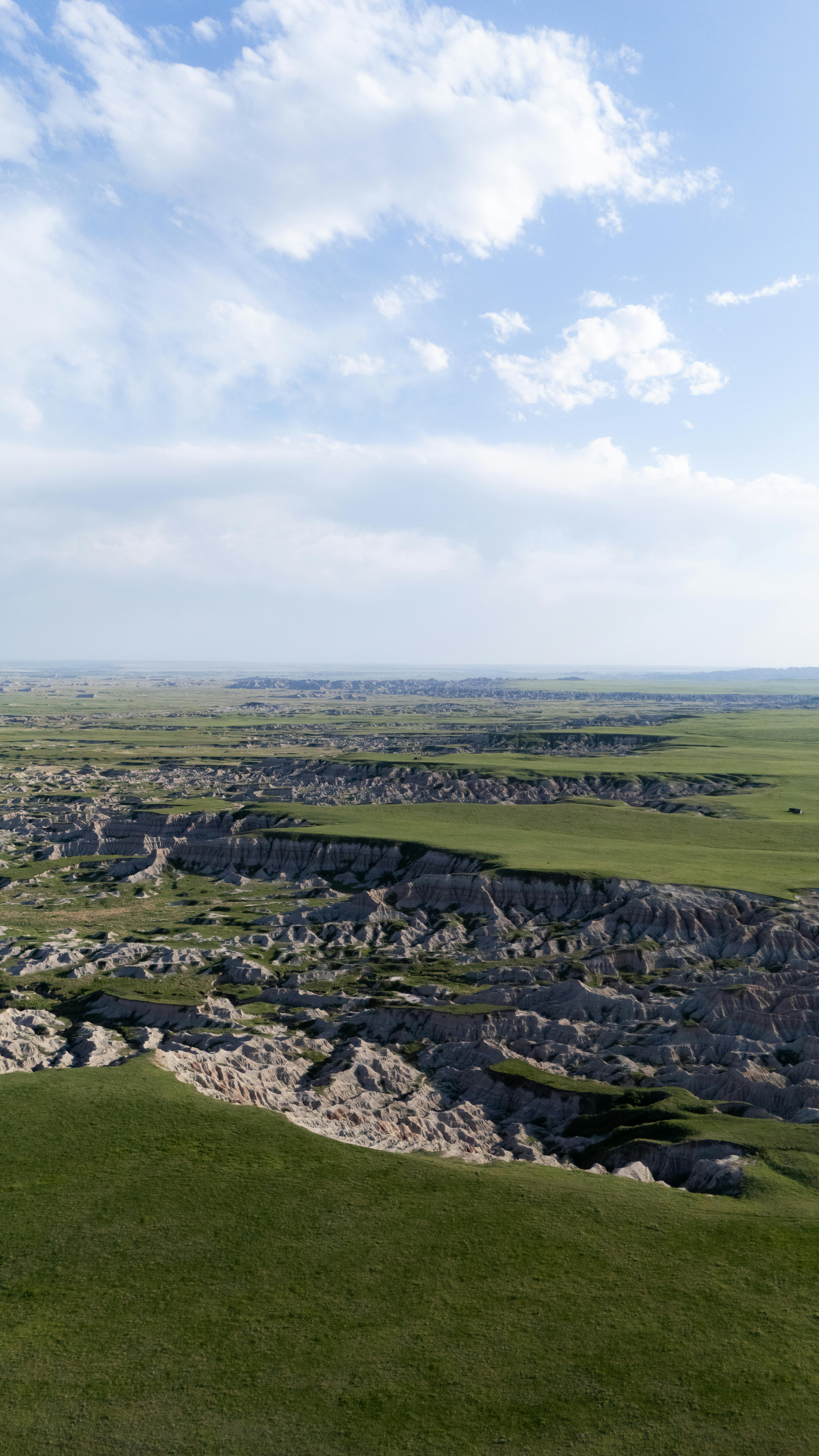 grátis Paisagem aérea de Badlands com pastagens e formações naturais sob um céu azul. Foto profissional