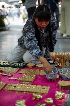 Street vendor arranging handmade jewelry on display in a vibrant outdoor market setting.