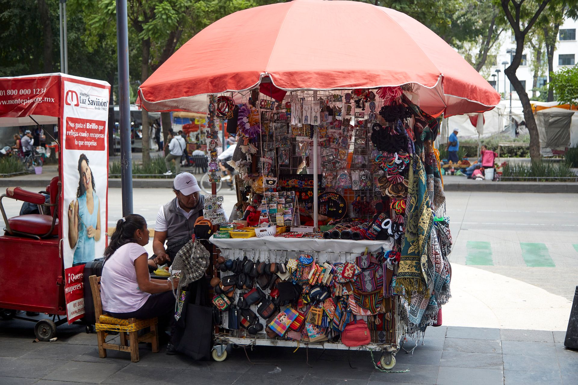 Colorful street market vendor in a bustling urban setting under a red umbrella.
