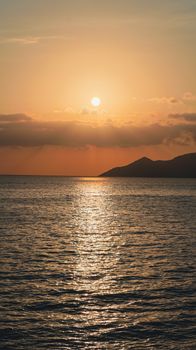 A tranquil ocean sunset view with mountains on the horizon and golden reflections on water.