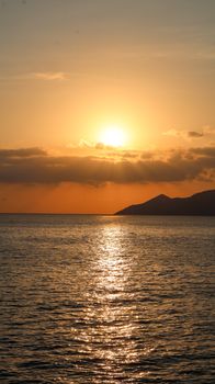 A tranquil ocean sunset with vibrant colors and a mountain silhouette creates a peaceful scene.