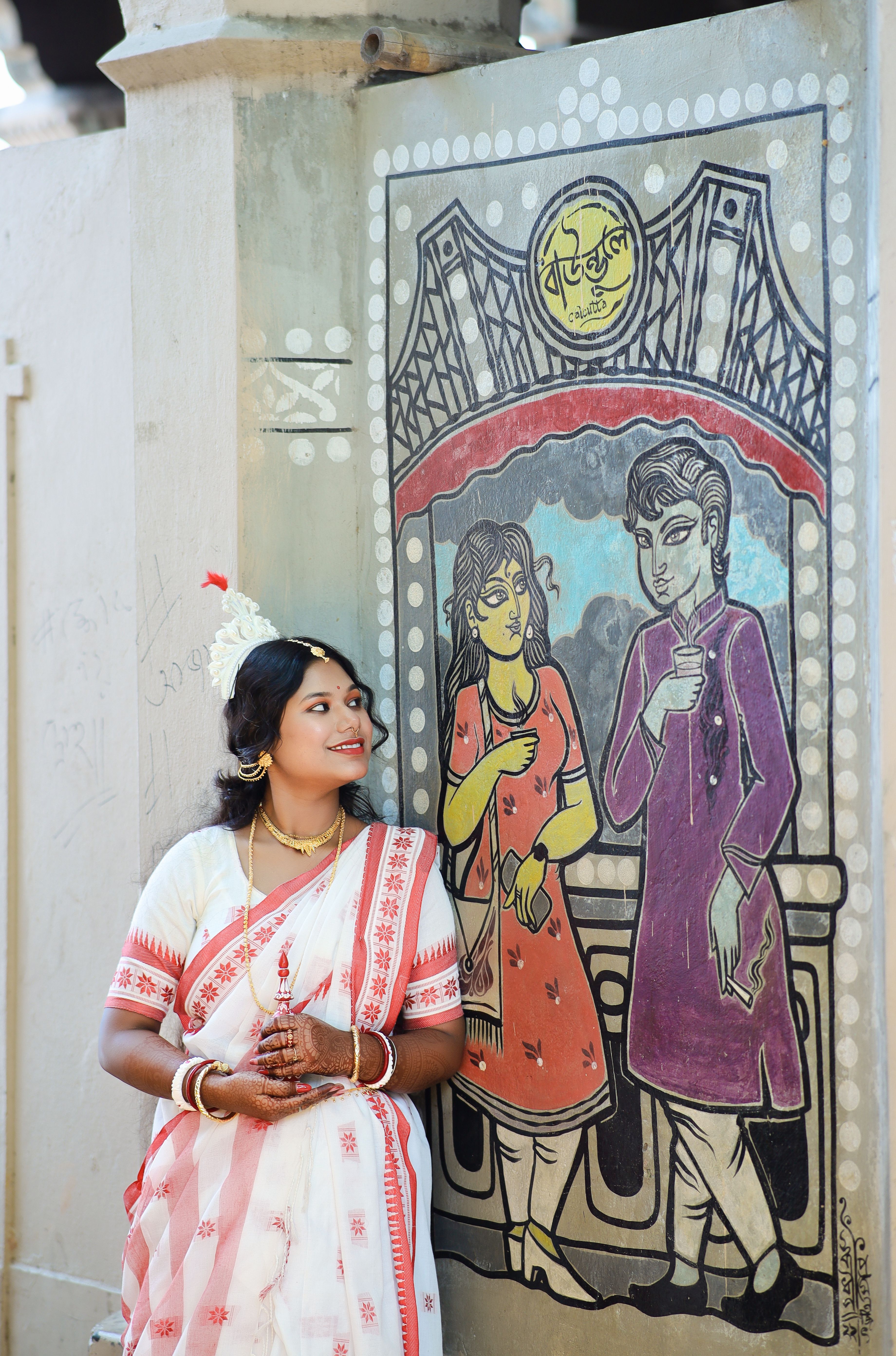 Woman in white and red saree posing by colorful wall mural. Traditional Indian attire.