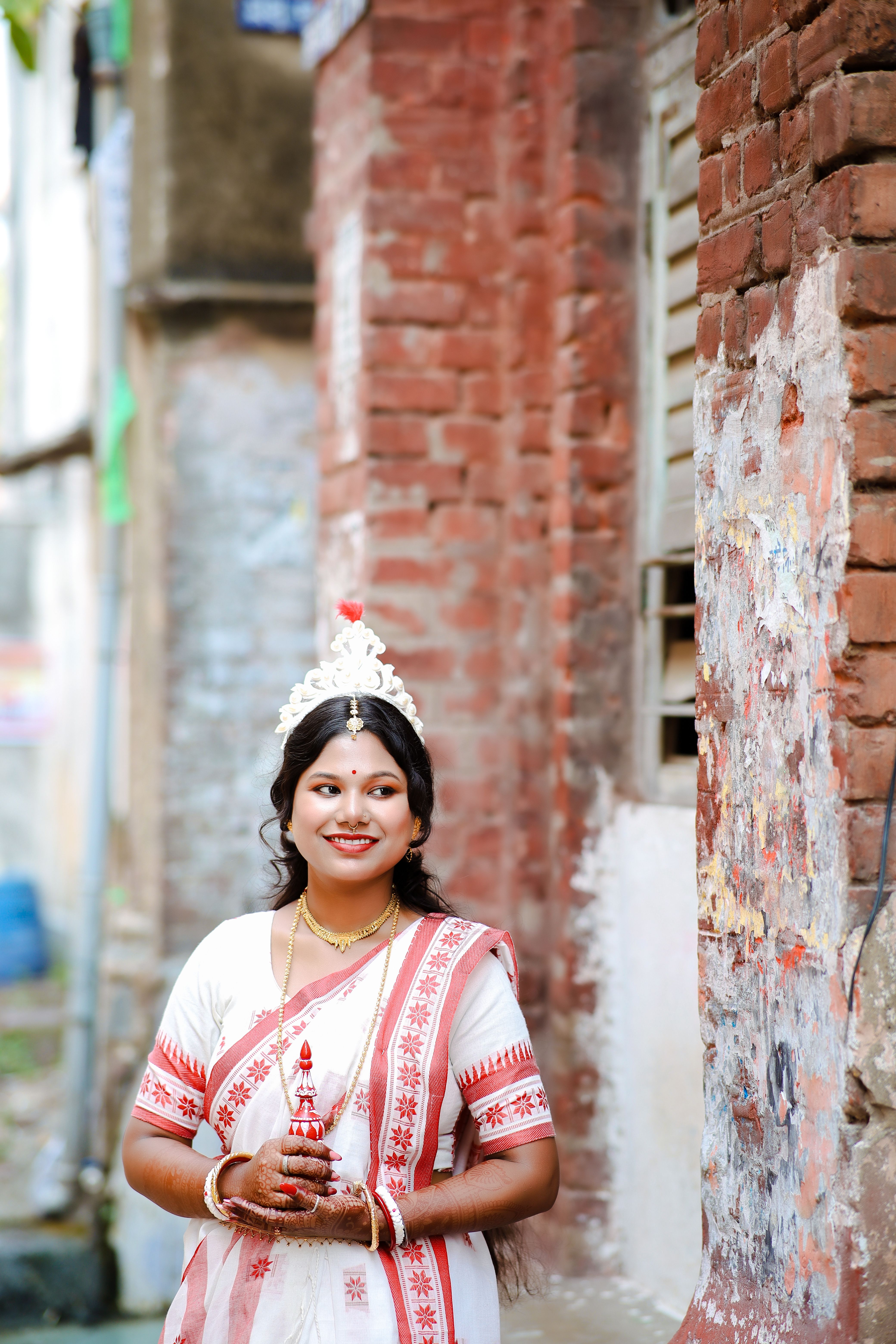Smiling Bengali bride in a red and white sari, adorned with traditional ornaments.
