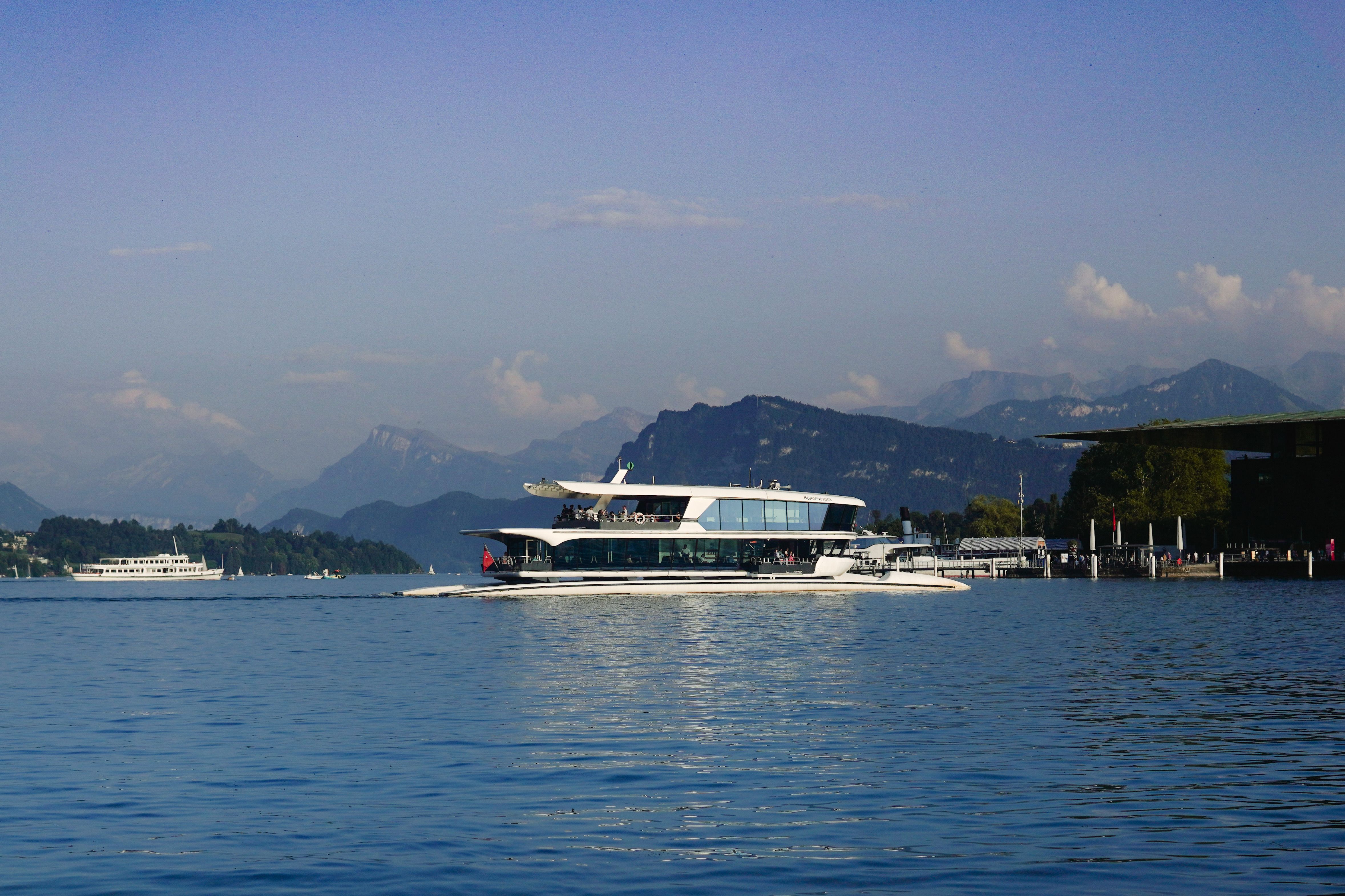 Sleek modern boat cruising a lake with snow-capped mountains behind it.