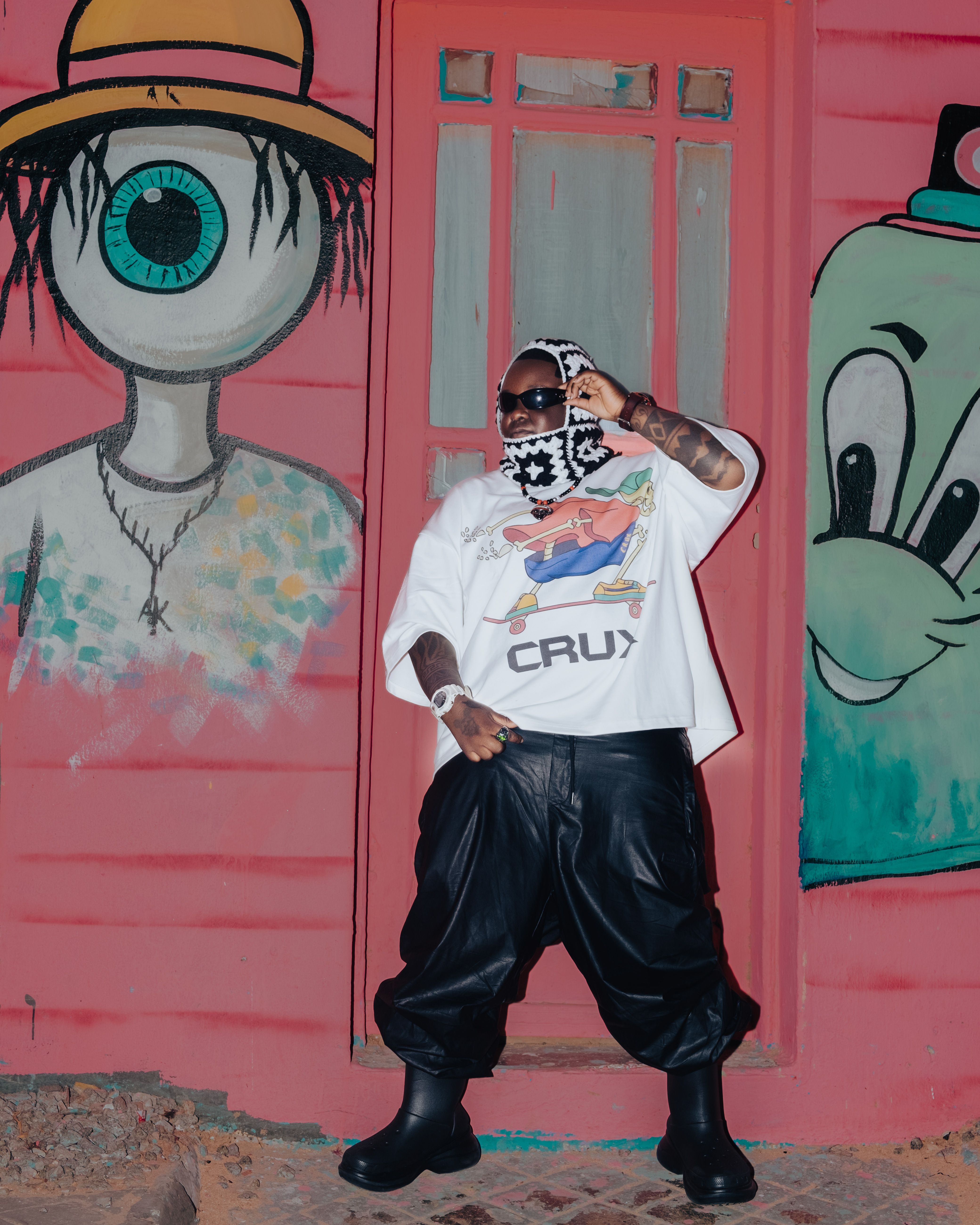 Person posing with unique street fashion against vibrant graffiti backdrop, showcasing urban culture.