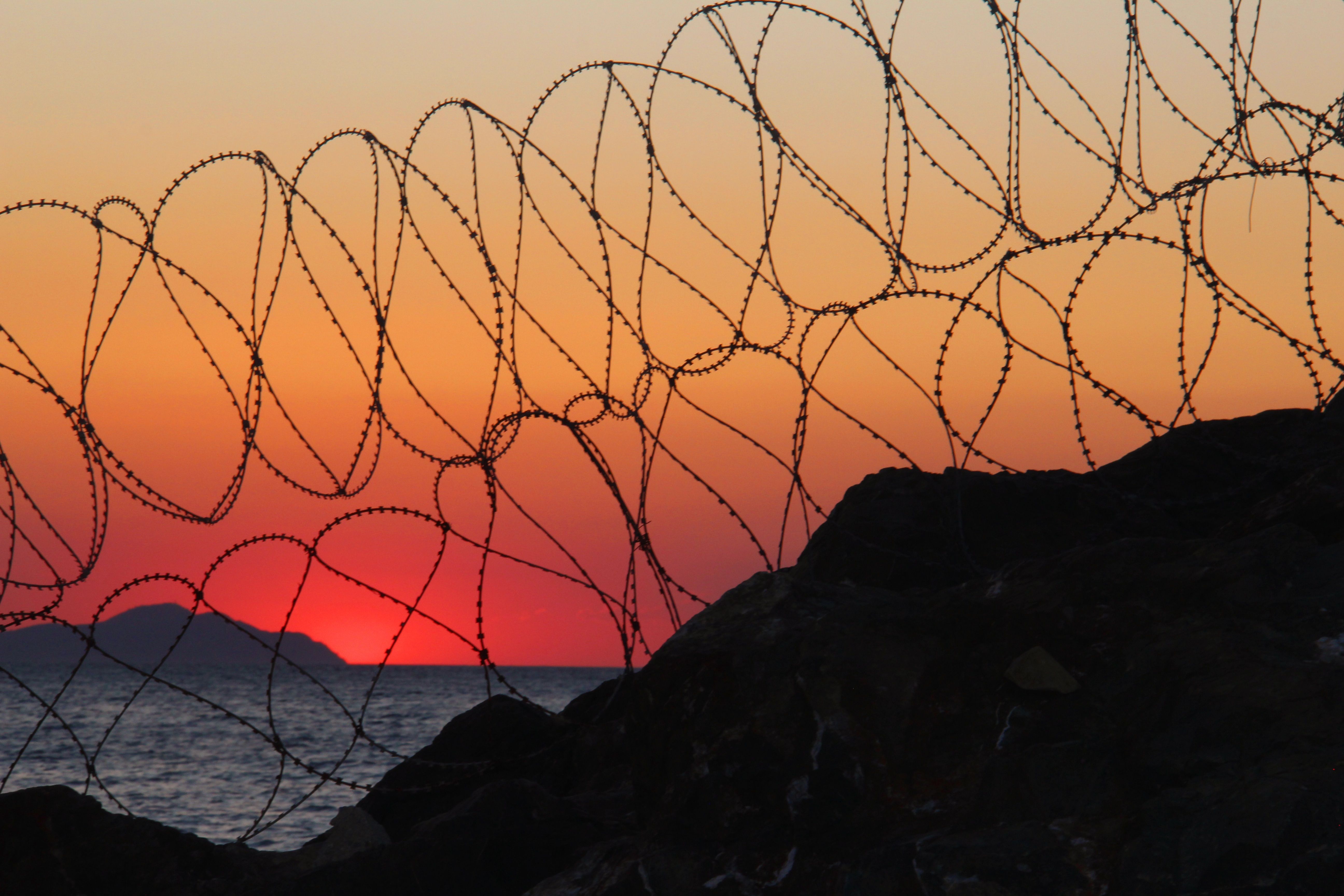 Dramatic Sunset Silhouette Behind Barbed Wire · Free Stock Photo