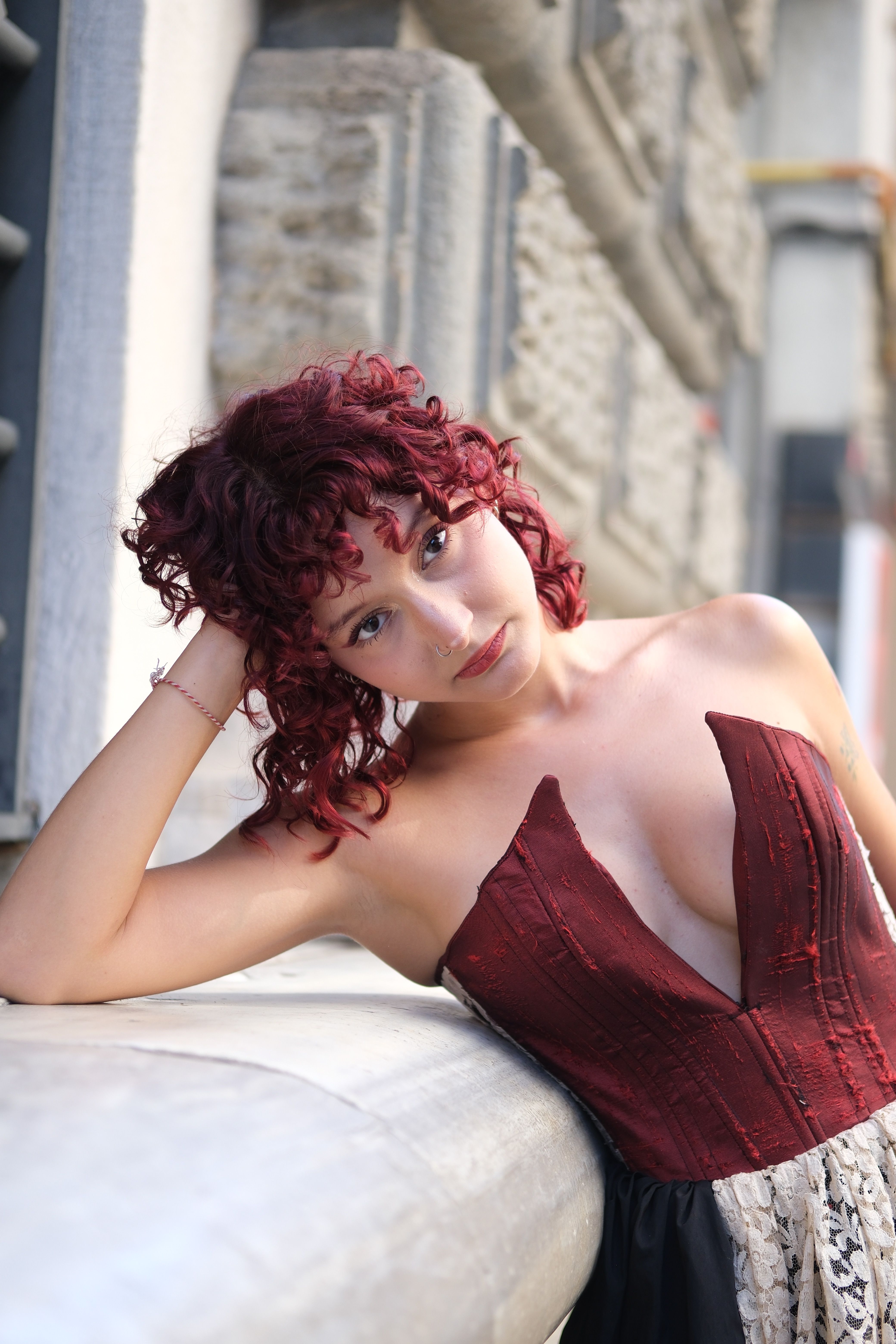 Stylish woman with curly hair in urban setting, leaning against wall.