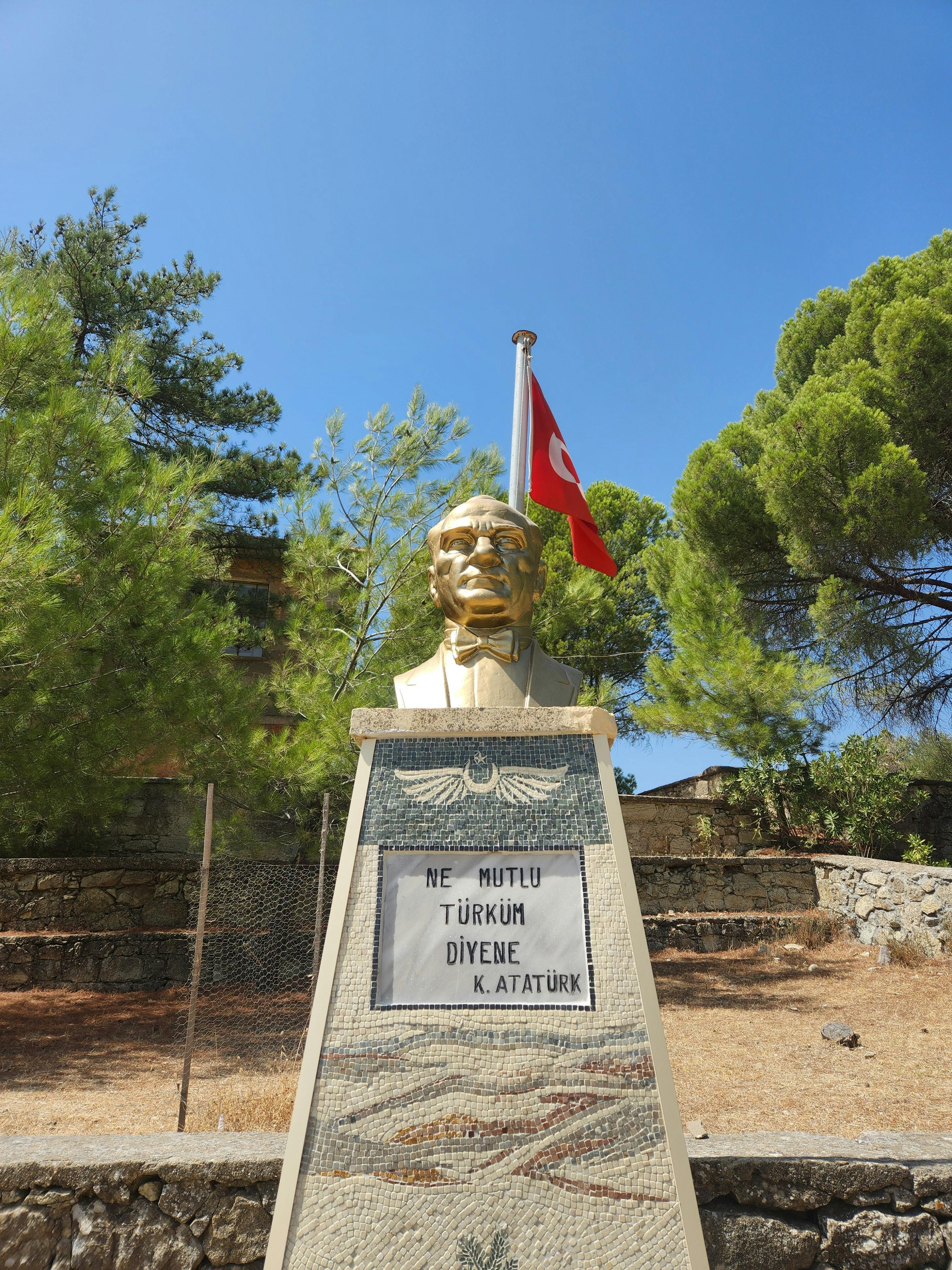 Bust of Atatürk with a Turkish flag in a serene outdoor setting.