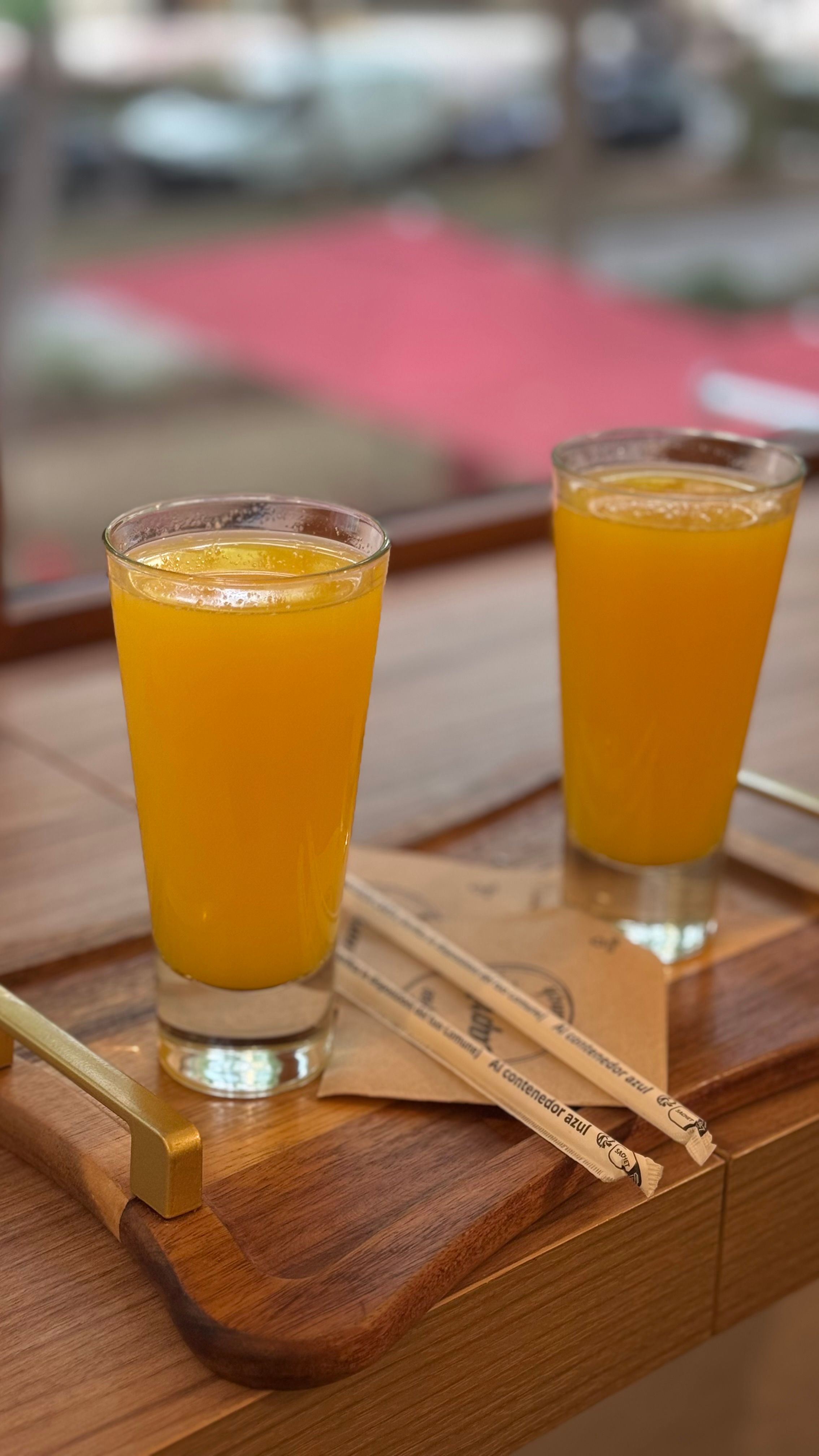 Two glasses of fresh orange juice on a wooden tray with straws indoors.