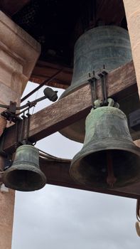 Dramatic view of large rustic bronze bells on a tower with cloudy sky.