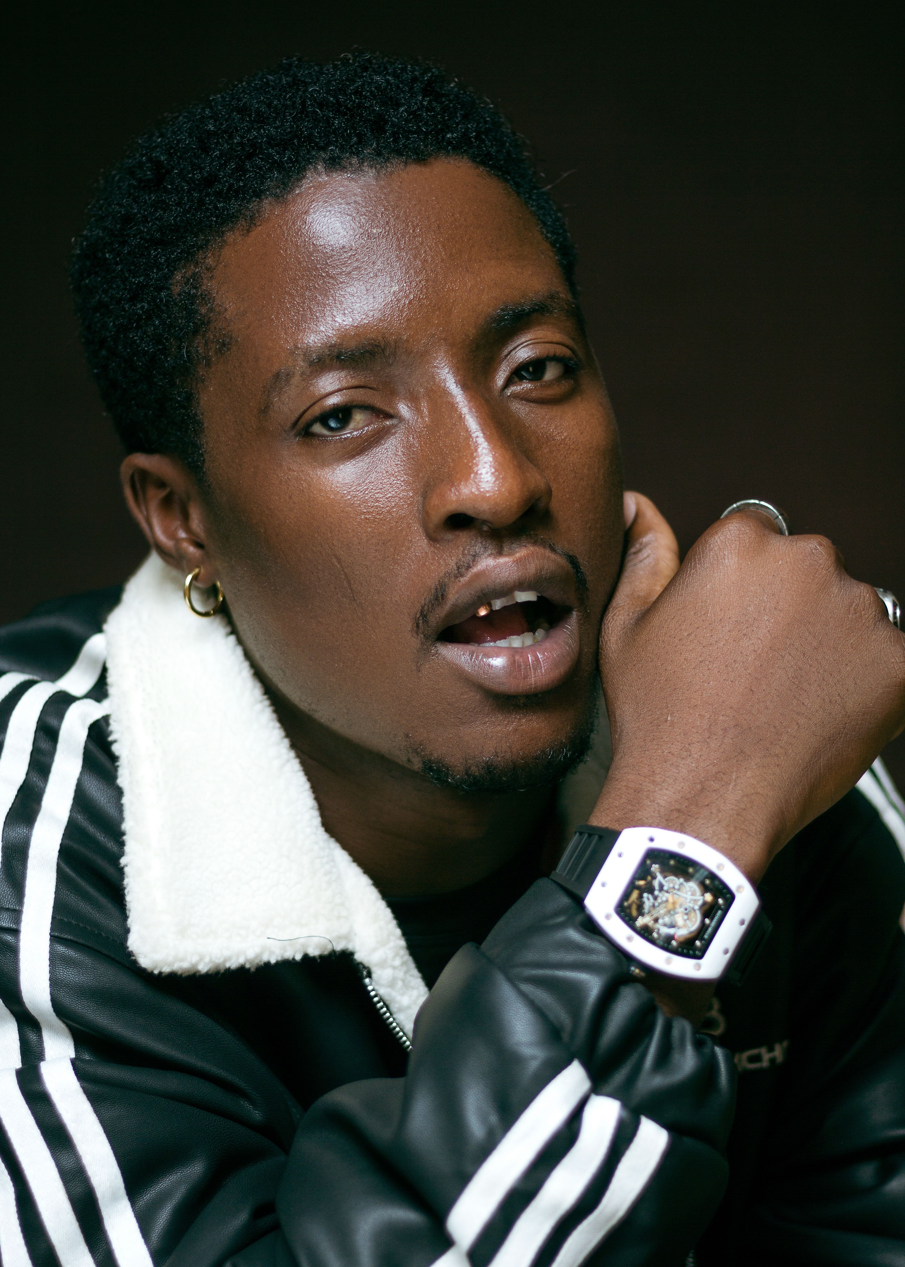 Close-up portrait of a stylish black man wearing a watch and jacket.