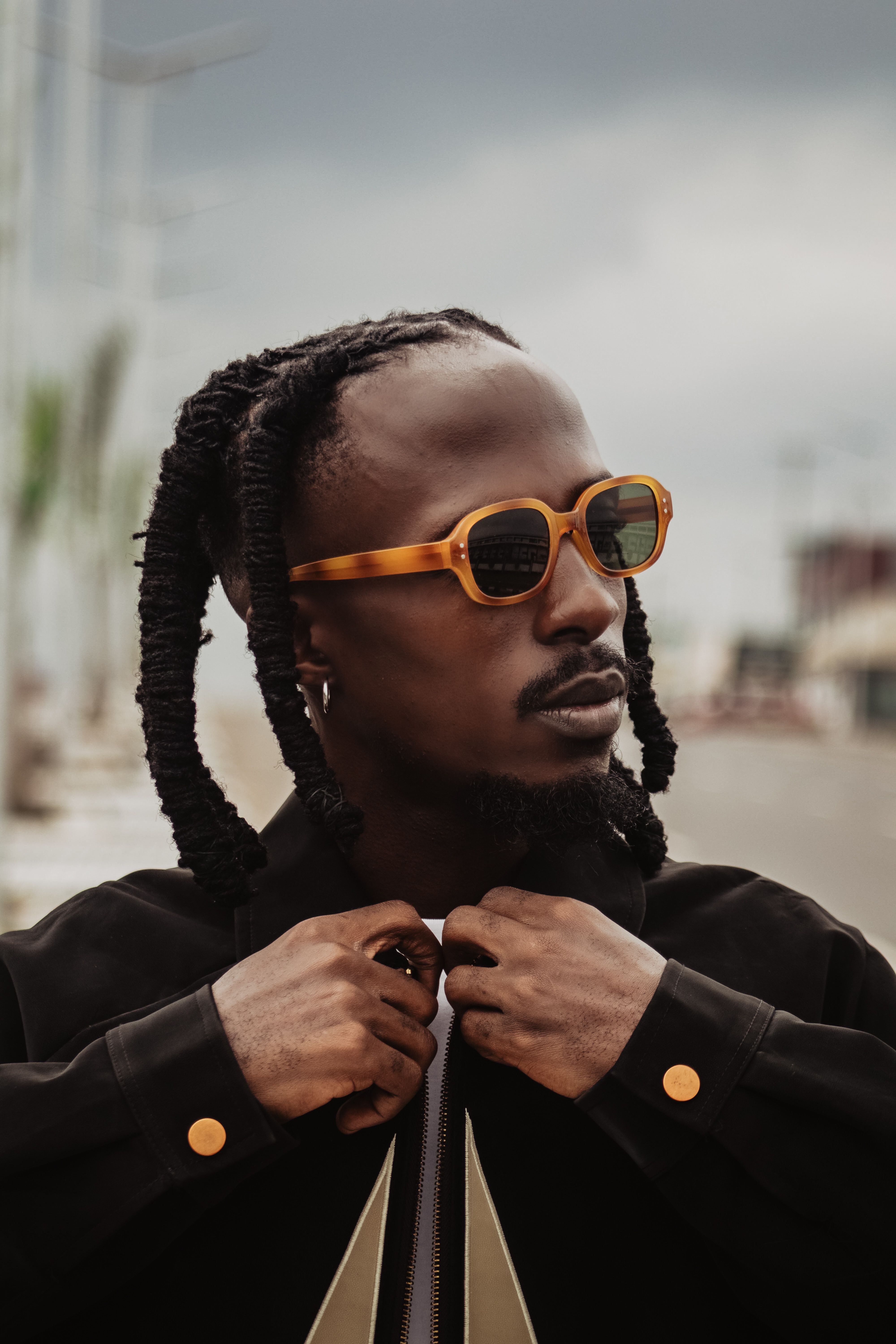 Confident man in sunglasses with unique hairstyle adjusting his jacket.