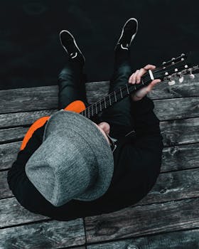 一位戴着软毡帽、背着吉他的音乐家正坐在木码头上享受休闲时光