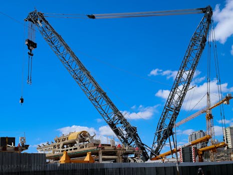Large tower cranes dominate a construction site under a bright blue sky, symbolizing urban development.