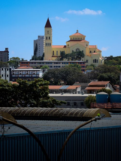 Free A vibrant church with a yellow facade stands amidst a modern urban landscape under a clear blue sky. Stock Photo