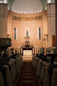 An elegant church interior set for a wedding, featuring floral decorations and religious artifacts.
