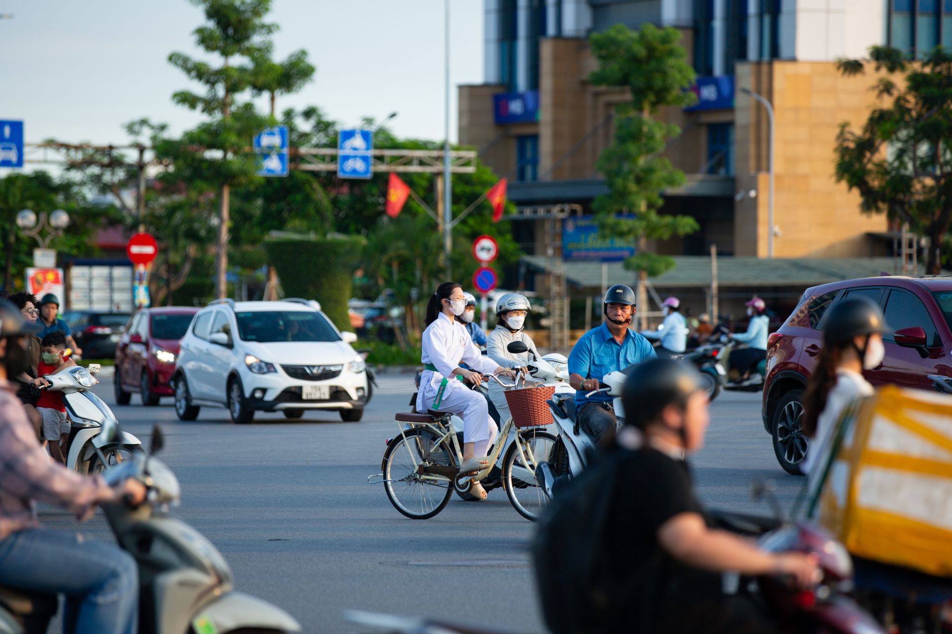 A busy city street with people on bikes and scooters navigating through traffic during the day.