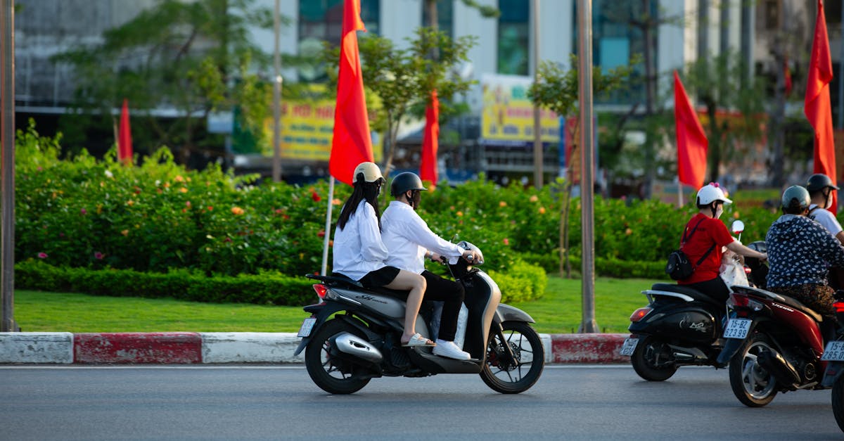 A group of people riding scooters on an urban road lined with red flags, indicating a vibrant city scene.