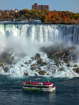 A vibrant tourist boat navigates close to the stunning Niagara Falls during autumn.