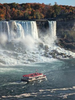 Stunning view of Niagara Falls with a crowded tour boat in autumn.