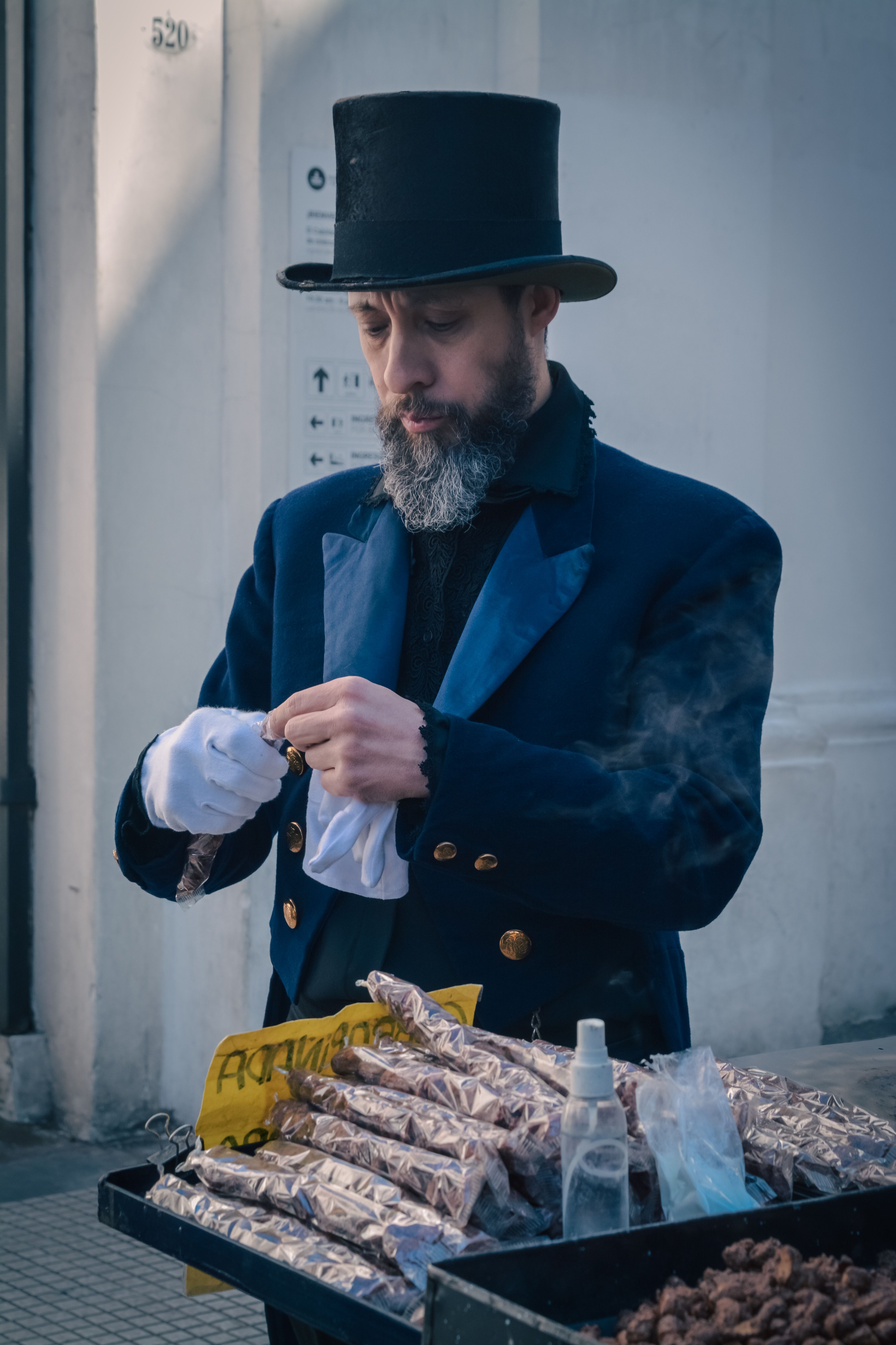 Street vendor in vintage top hat and coat sells roasted nuts outdoors.