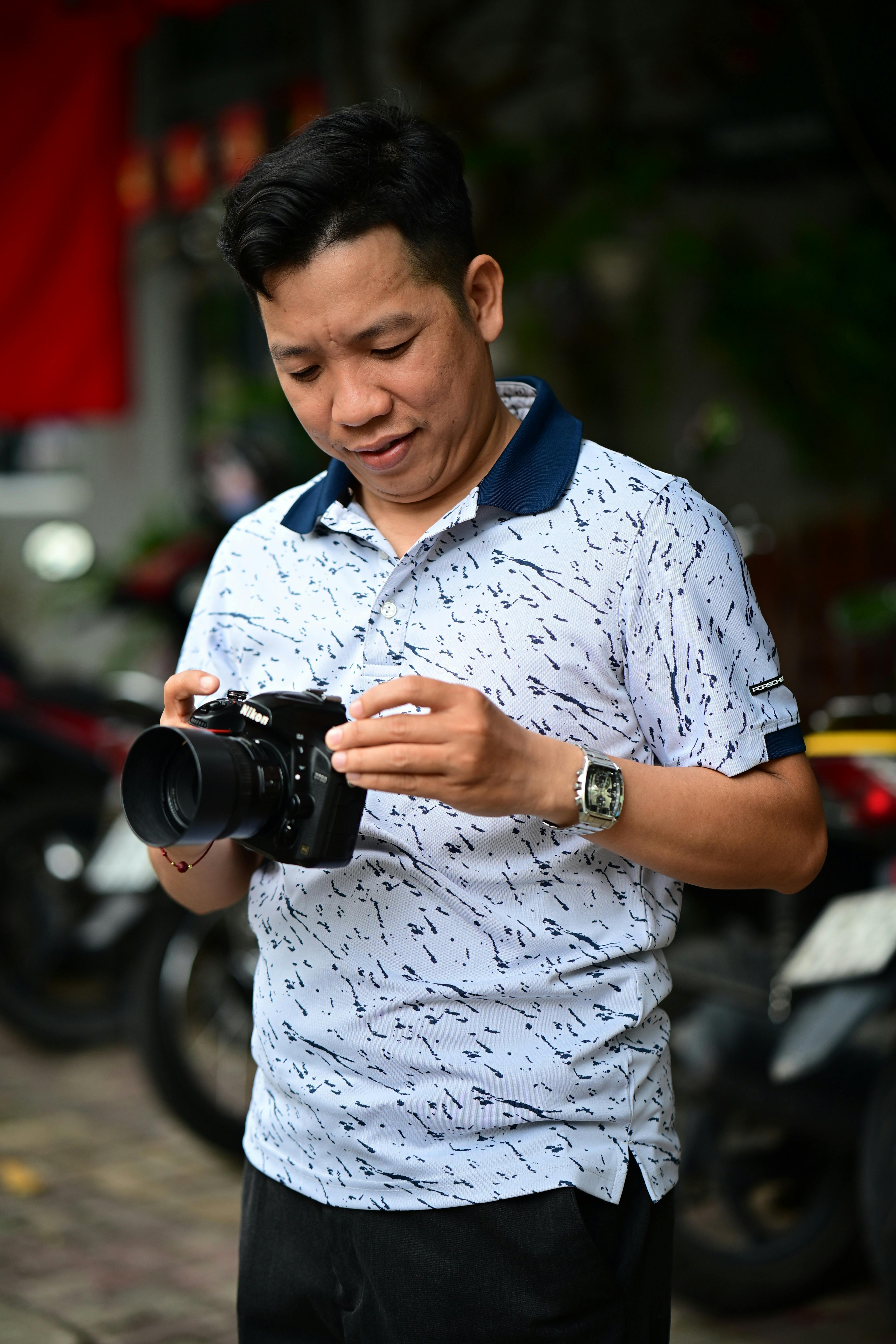 grátis Homem em traje casual examinando uma câmera DSLR ao ar livre, demonstrando interesse em fotografia. Foto profissional