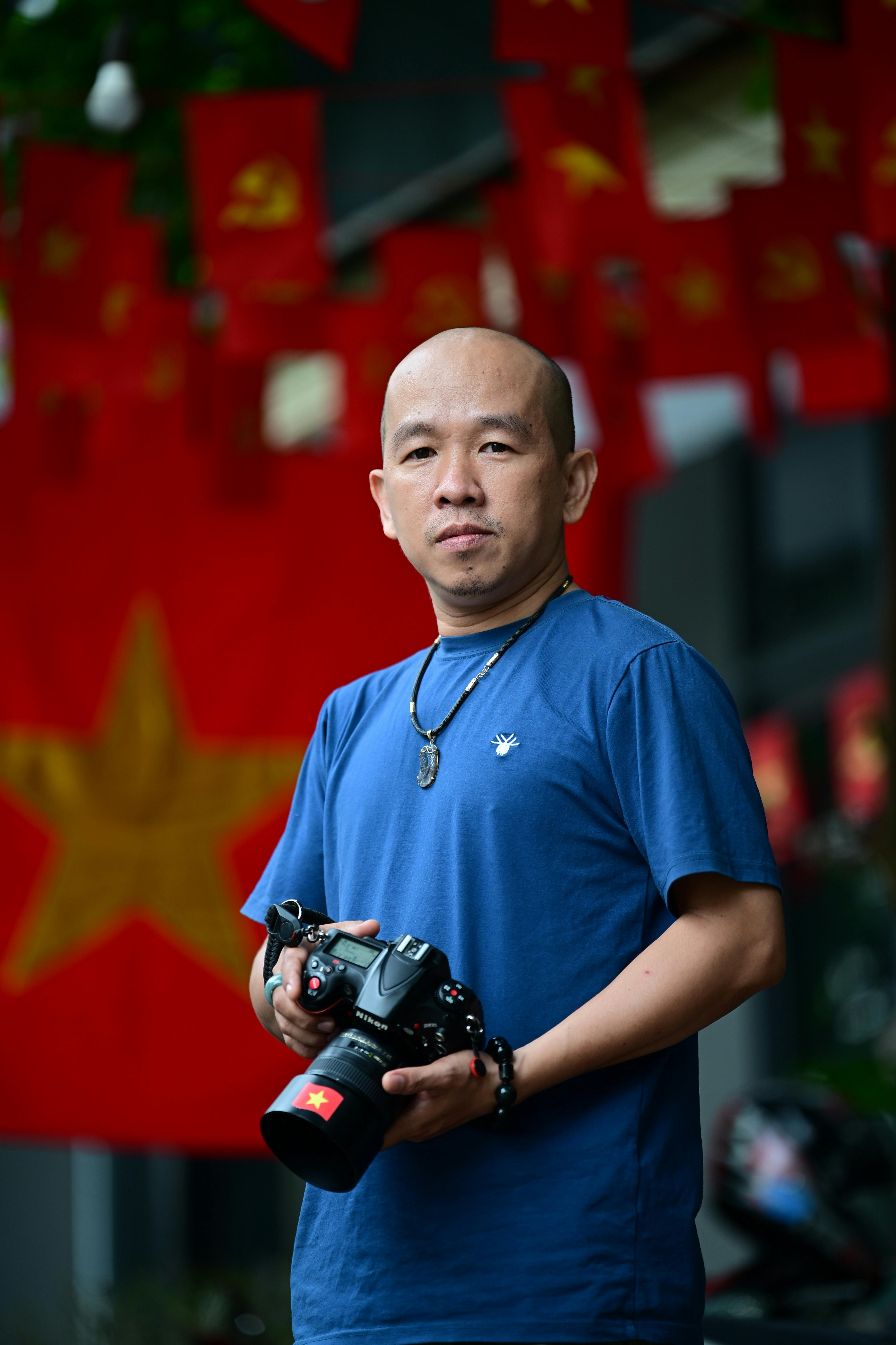 Man holding camera in front of Vietnamese flags, outdoors setting.