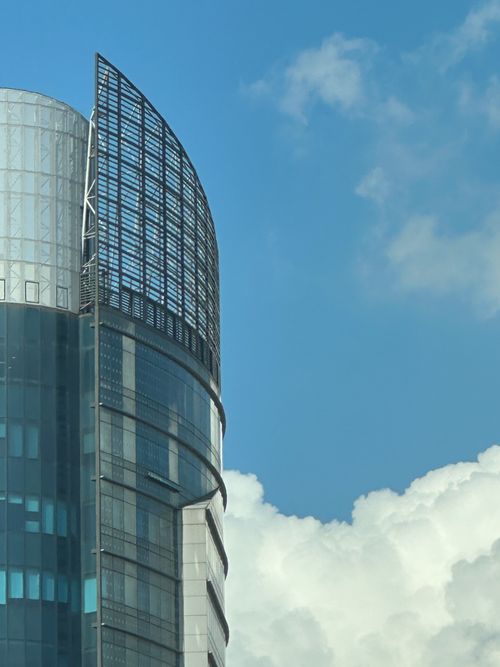 Free Modern skyscraper with reflective glass facade against a blue sky and clouds. Stock Photo