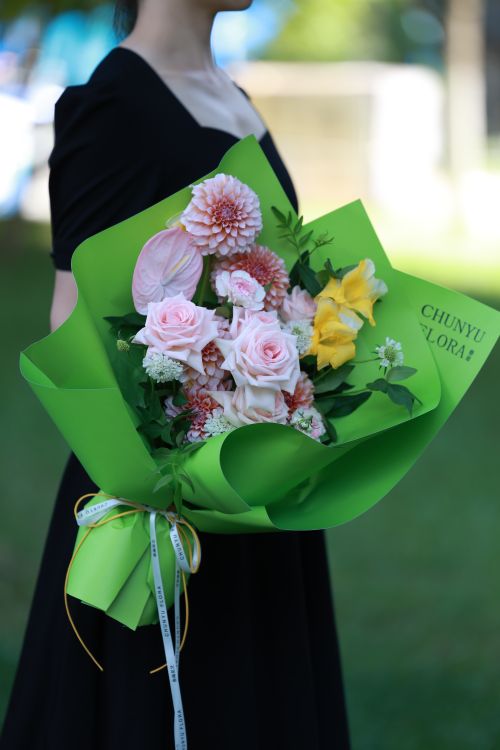 Free A beautiful bouquet of roses and dahlias wrapped in green paper, held by a person in a black dress. Stock Photo