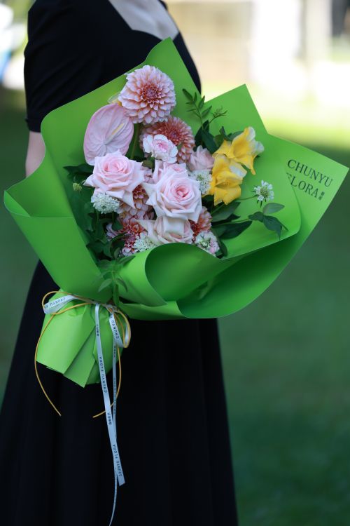 Free A stylish flower bouquet with green wrapping, held outdoors by a person in a black dress. Stock Photo