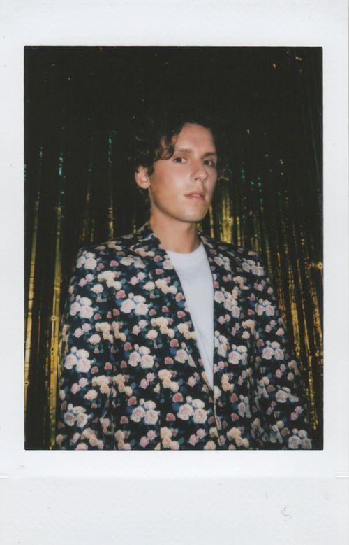 Free Stylish young man posing in floral jacket against golden drape, embodies modern fashion. Stock Photo