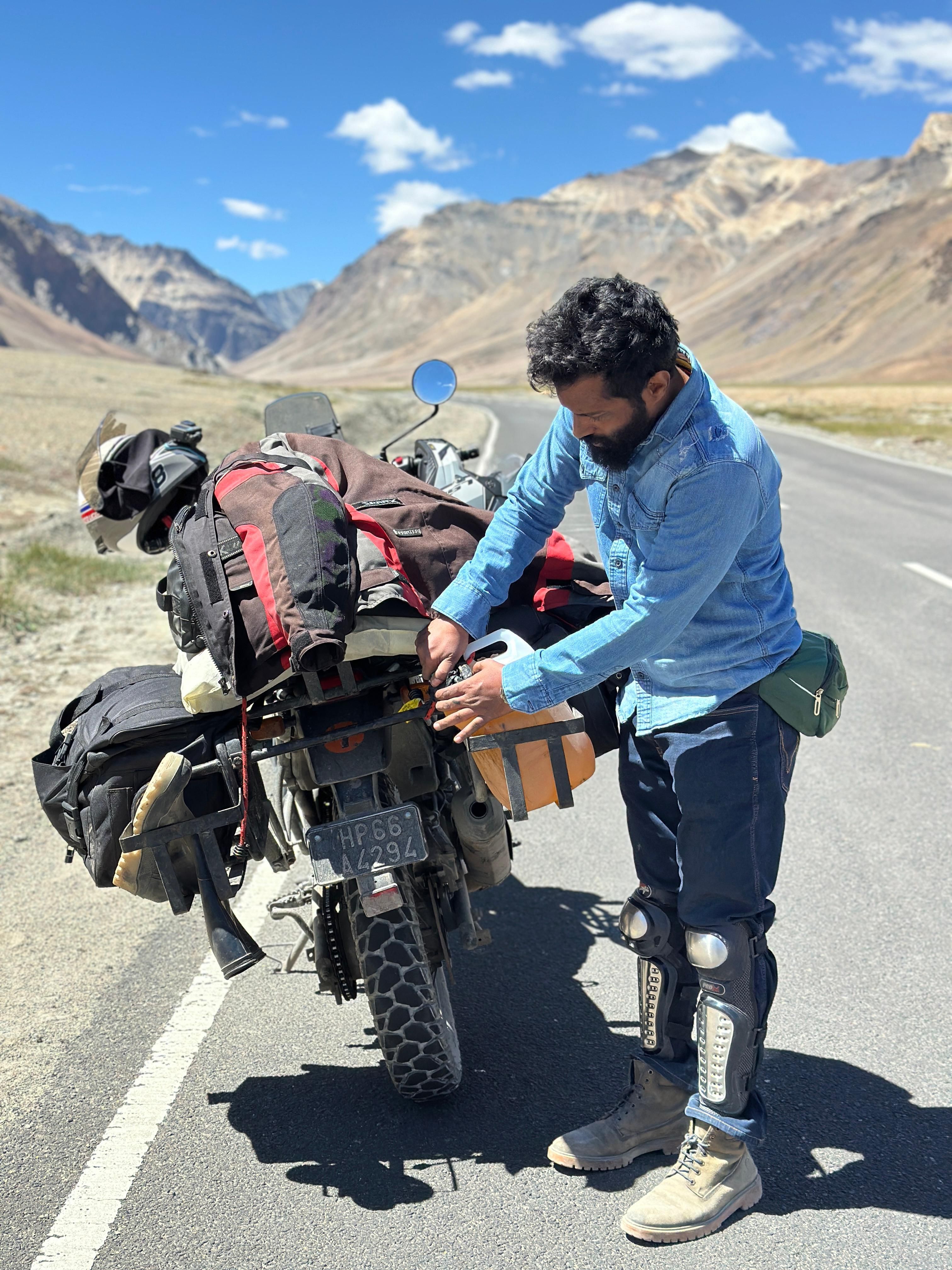 Rider adjusting gear on a motorcycle during a scenic road trip in Leh, India.
