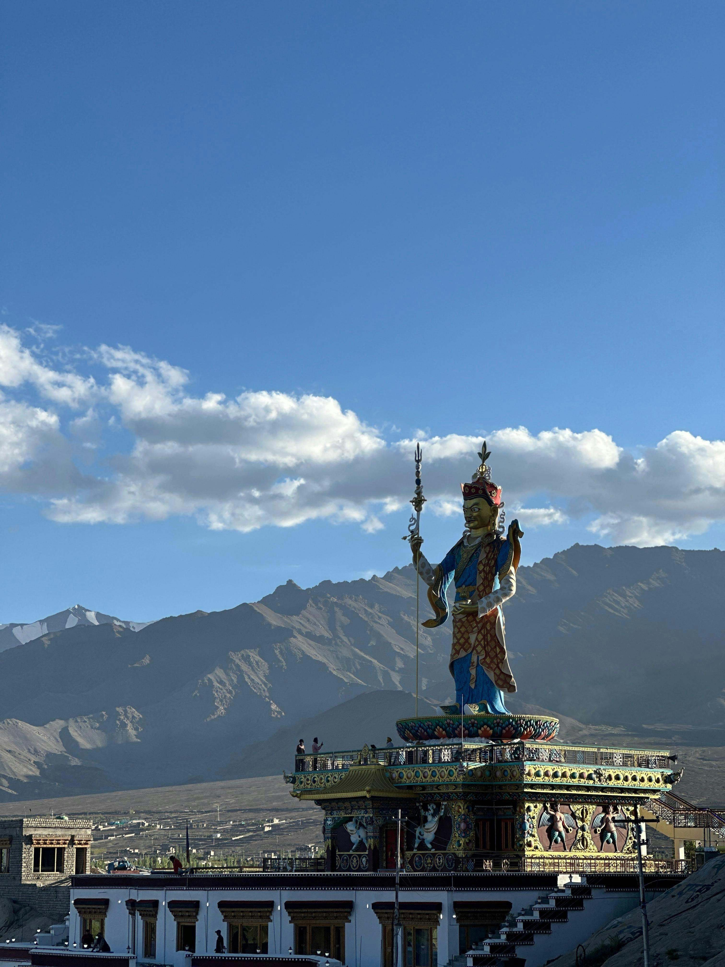 Majestic Buddhist statue stands tall against the backdrop of the Leh Himalayas, under a clear blue sky.