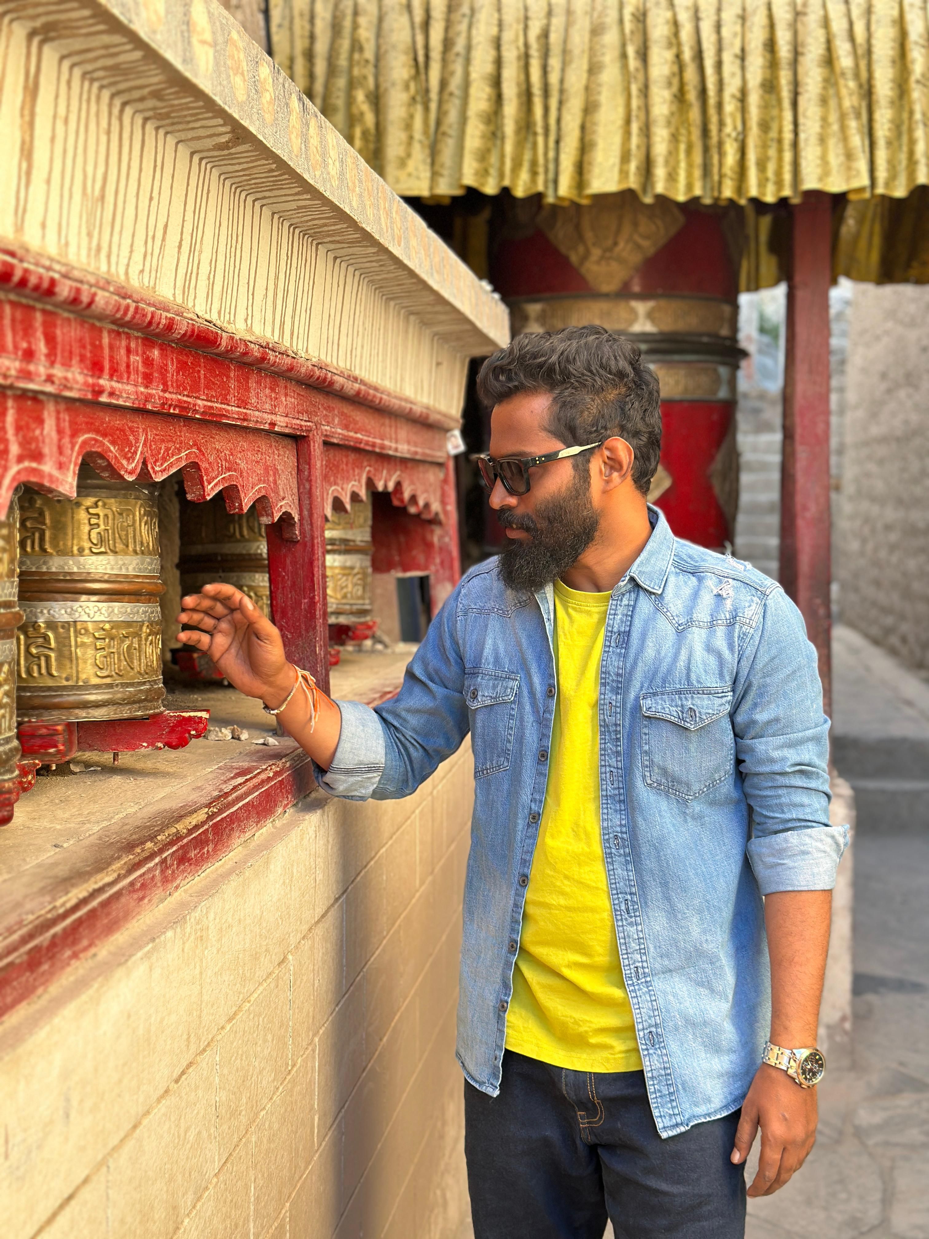 A man interacting with prayer wheels in a temple in Leh, Ladakh, showcasing traditional architecture.