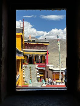 Discover the vibrant architecture of a Leh monastery, framed by a window under a bright blue sky.
