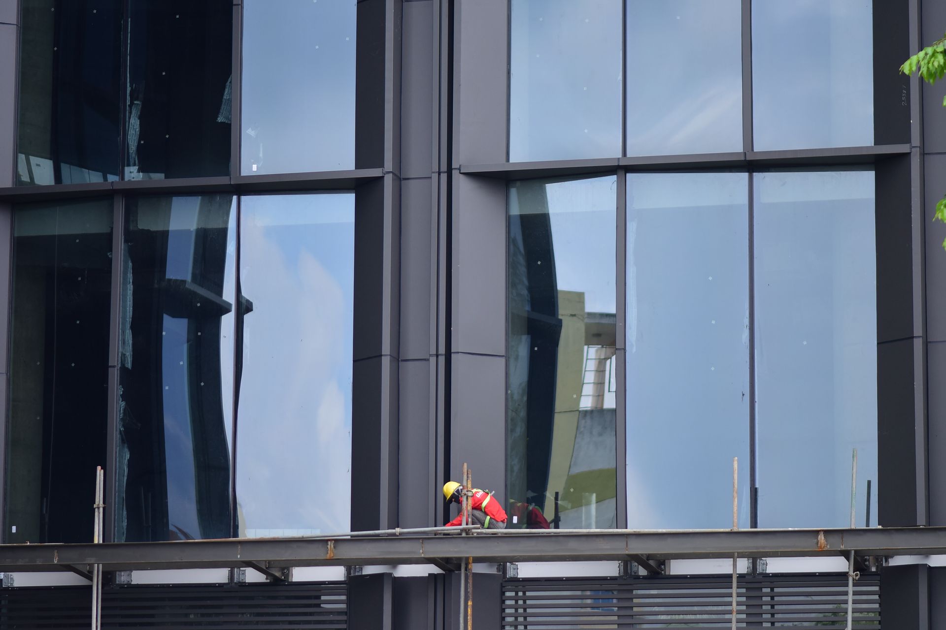 Worker in safety gear on a skyscraper facade scaffolding.