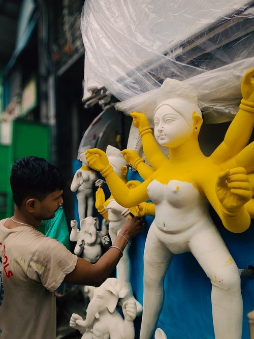 Free Young artist meticulously painting a Hindu goddess statue in an outdoor artisan workshop. Stock Photo