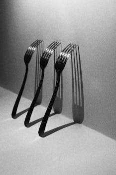 一幅黑白艺术图像中，叉子在极简主义静物上投下阴影