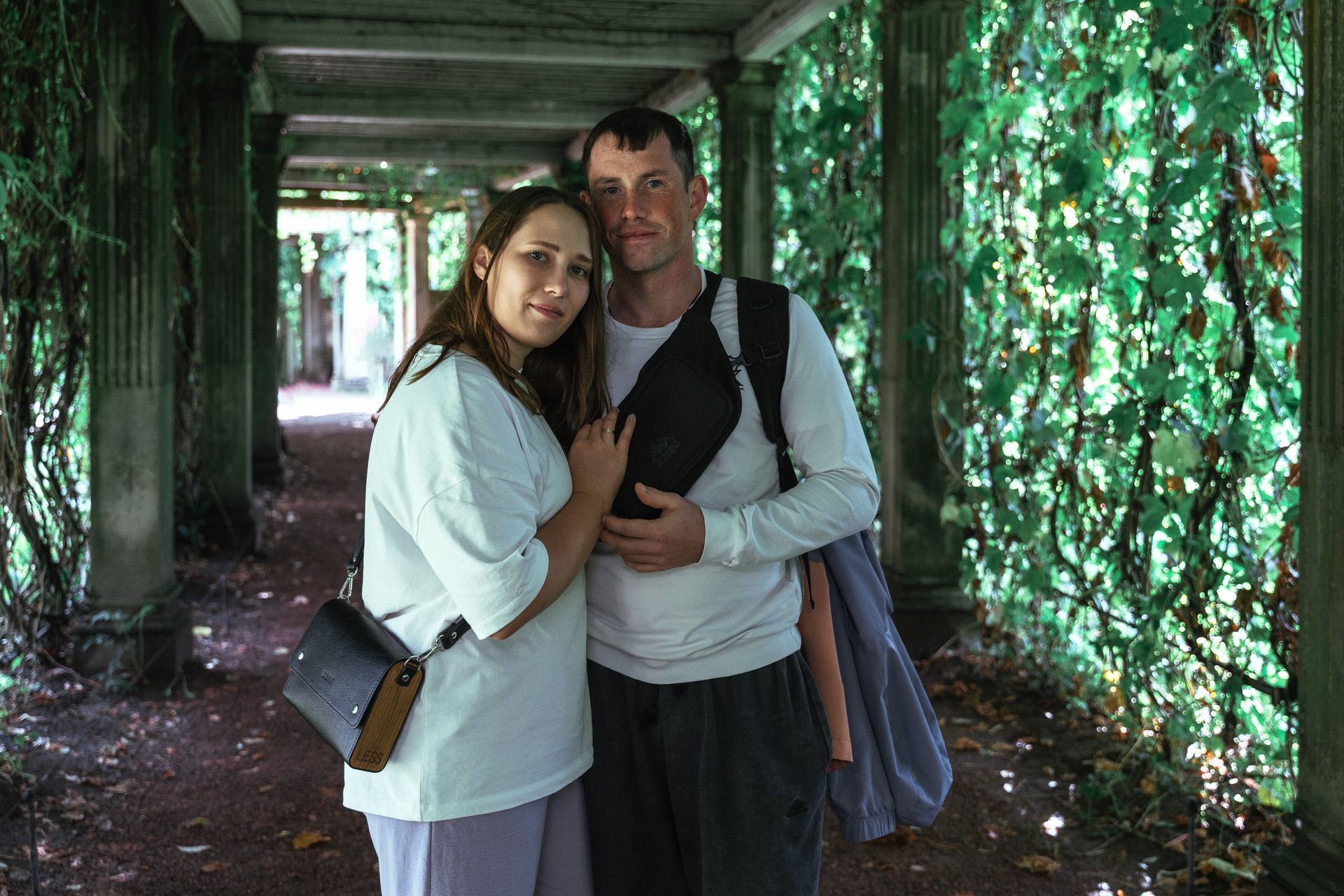 A loving couple stands in an ivy-draped passageway under natural light.