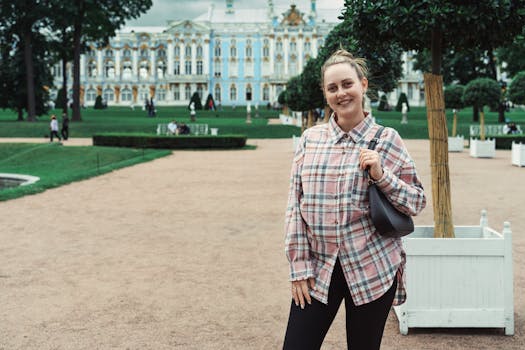 Smiling woman in plaid shirt standing in front of the ornate Catherine Palace gardens.
