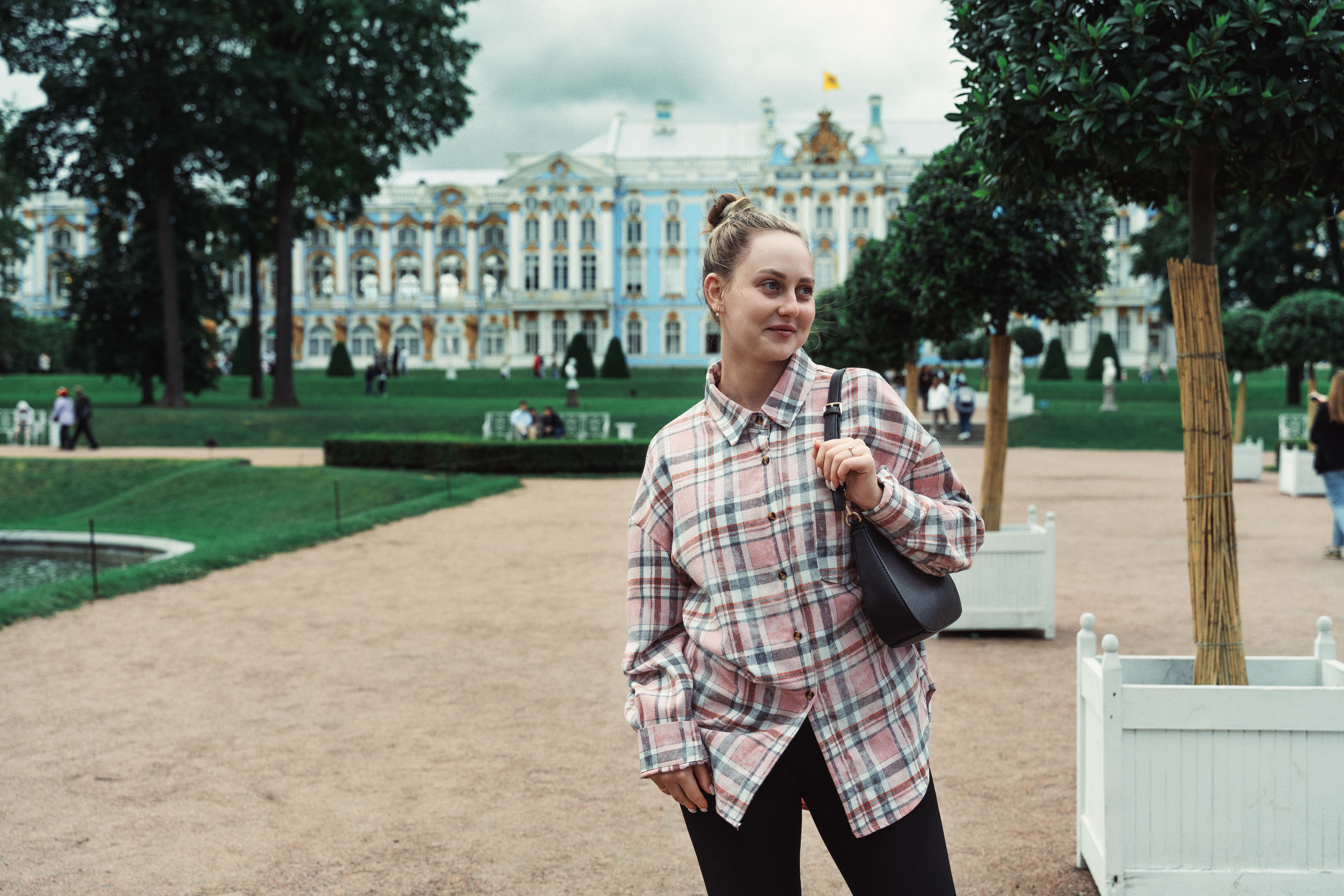 Young woman in plaid shirt posing outside Catherine Palace, showcasing the palace's beautiful architecture and lush gardens.