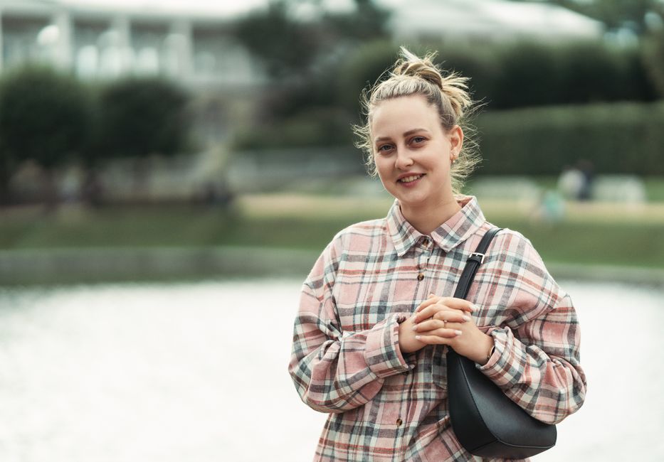5 Dicas para Cultivar a Autenticidade na Moda Pessoal 2 A woman in casual attire standing by a lake smiling outdoors, conveying a relaxed mood.