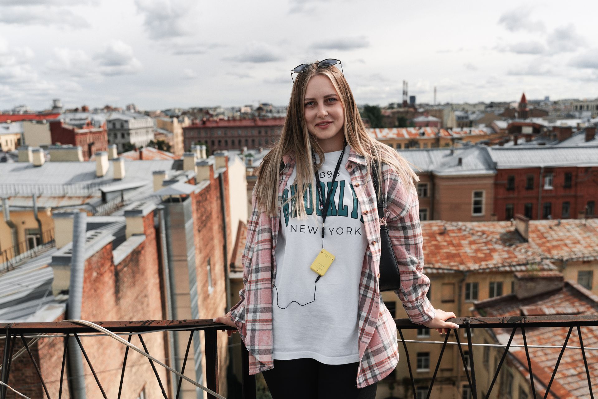 A happy woman enjoys a rooftop view of historic city architecture under a cloudy sky.