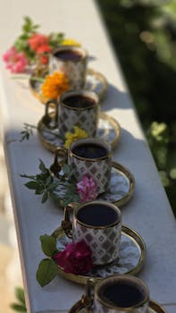 A row of ornate cups with Turkish coffee and flowers in an outdoor setting.