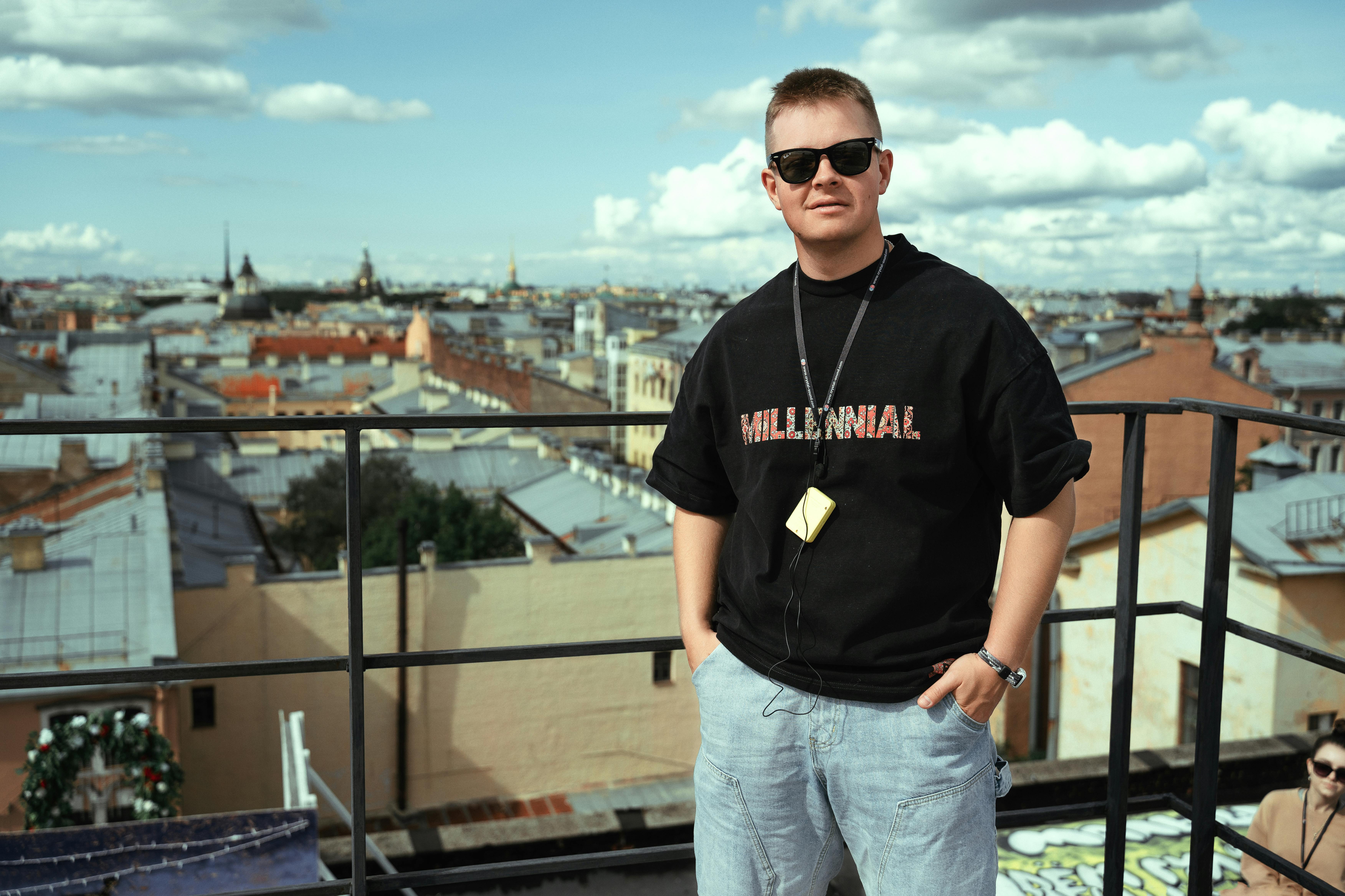 Young man in sunglasses posing confidently on a rooftop with a panoramic city view.