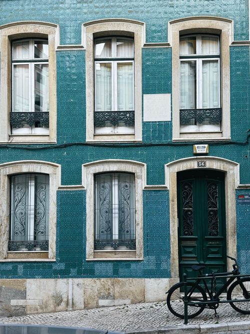 Free A classic blue-tiled building exterior in Lisbon with a parked bicycle, featuring ornate windows and a green door. Stock Photo