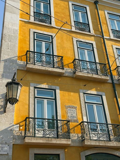 Elegant urban architecture featuring vibrant yellow facade with wrought iron balconies in daylight. — Intendente, Portugal.