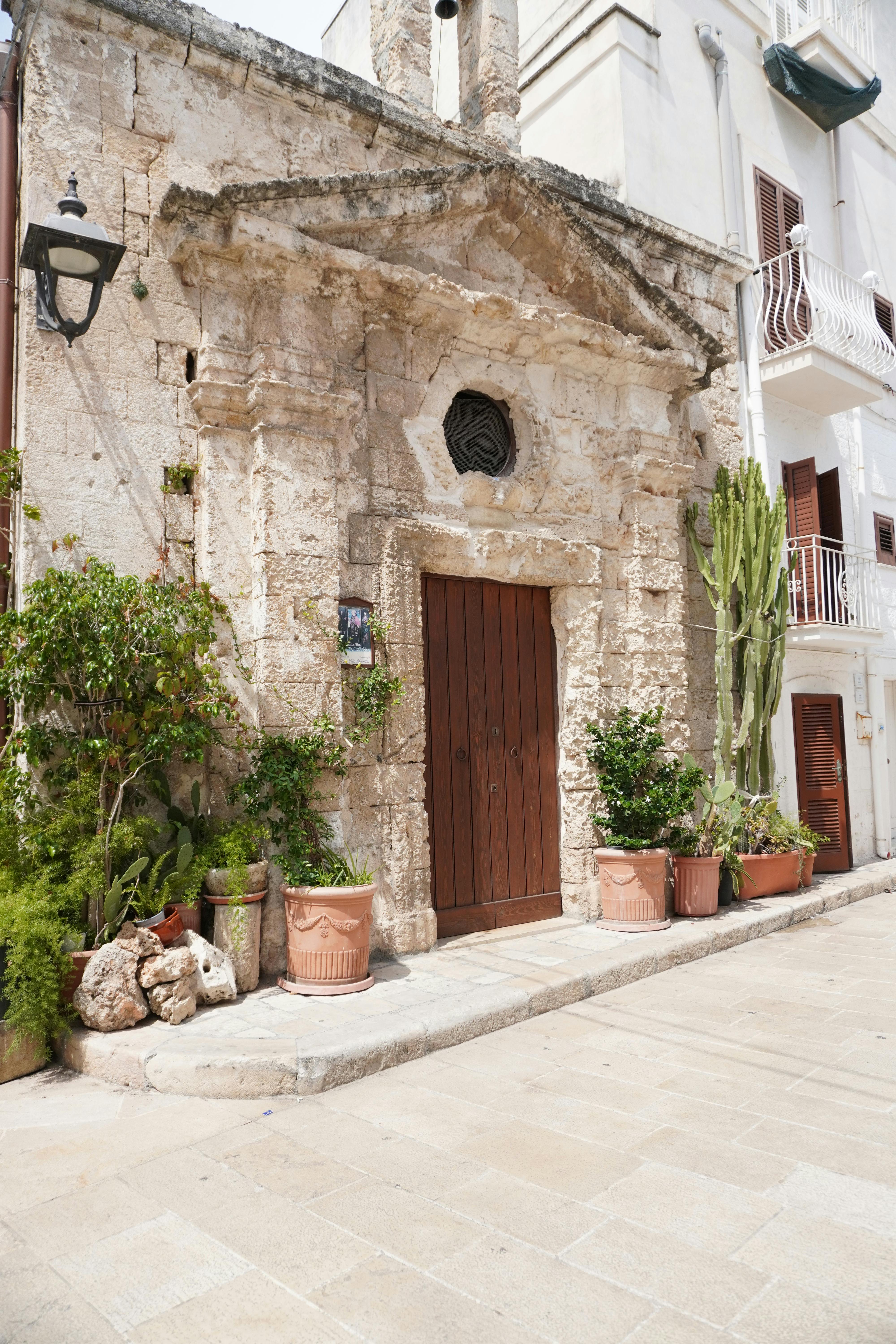 Ancient stone facade in Monopoli, Puglia with lush plants and wooden door.