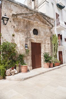 Ancient stone facade in Monopoli, Puglia with lush plants and wooden door.